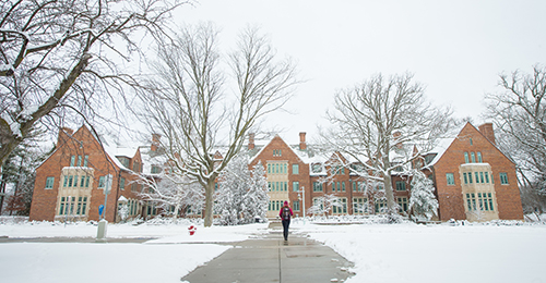 MSU building in winter with the lawn covered in snow and a student walking down the sidewalk