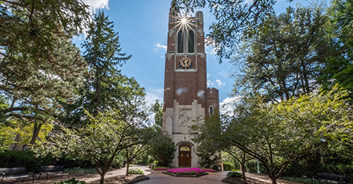 Beaumont Tower with flowers and the sun shining near the top